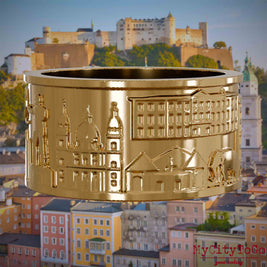 Vergoldeter Ring mit Reliefs bekannter Sehenswürdigkeiten der Stadt Salzburg. Den Hintergrund bildet eine Ansicht der Stadt Salzburg.