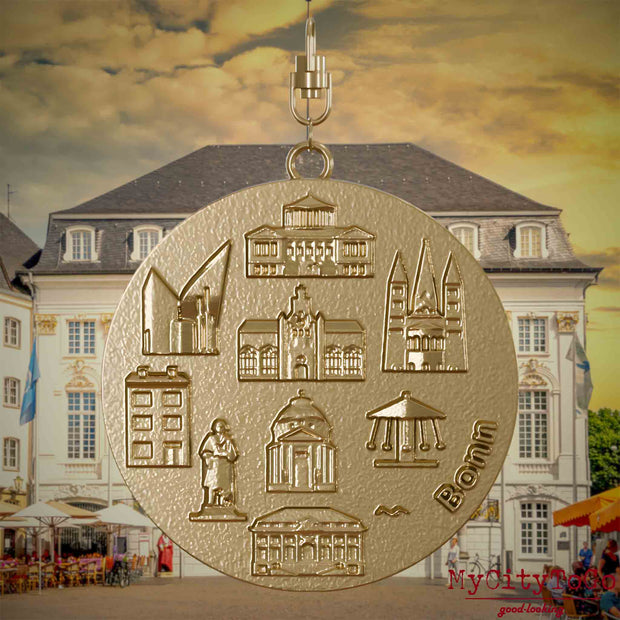 Halskette mit Drehwirbel und Vorderseite eines Schmuckanhängers aus vergoldetem Edelstahl, auf dem Reliefs bekannter Sehenswürdigkeiten der Stadt Bonn abgebildet sind. Den Hintergrund bildet eine Ansicht der Stadt Bonn.
