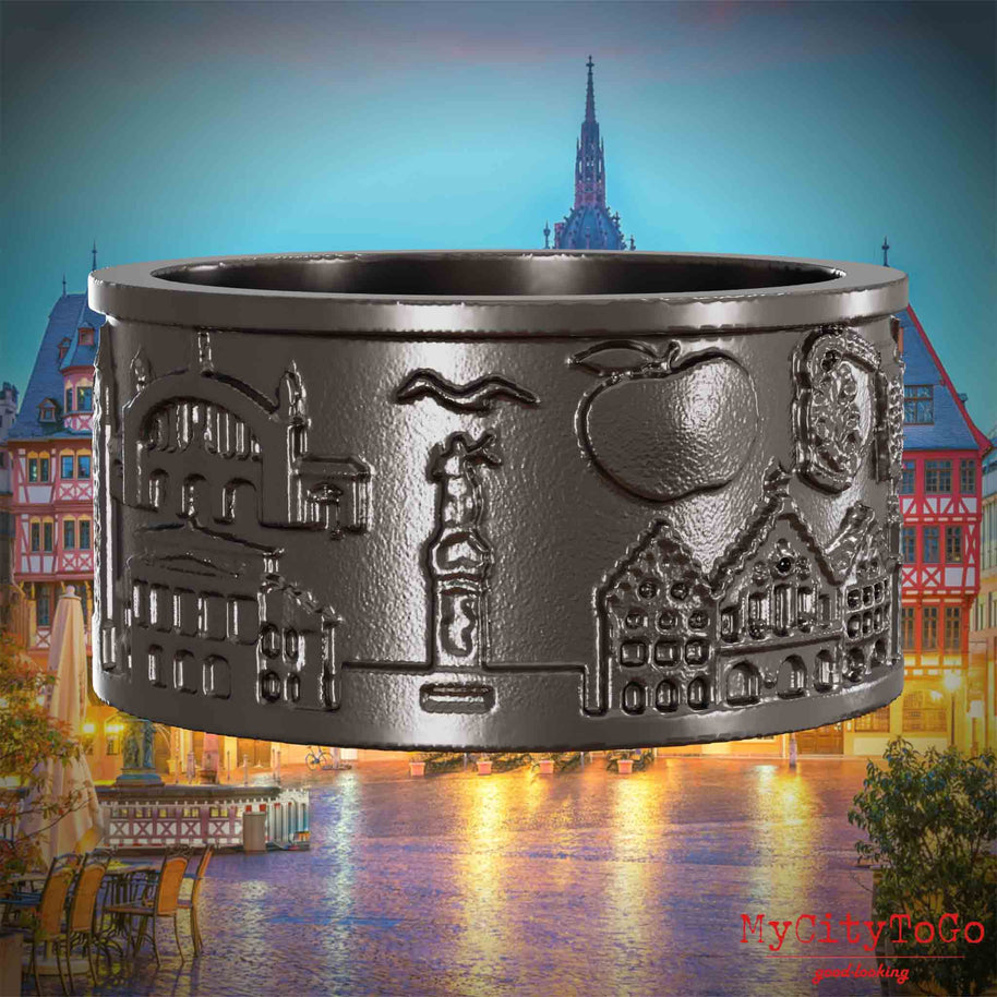 Ring aus Titan mit Reliefs bekannter Sehenswürdigkeiten der Stadt Frankfurt. Den Hintergrund bildet eine Ansicht der Stadt Frankfurt.