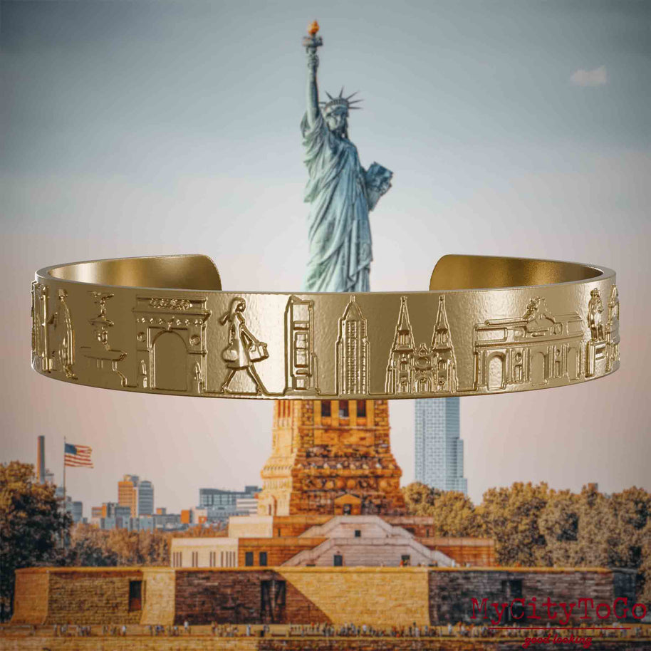 Armreif aus vergoldetem Edelstahl mit Reliefs bekannter Sehenswürdigkeiten der Stadt New York. Den Hintergrund bildet eine Ansicht der Stadt New York.