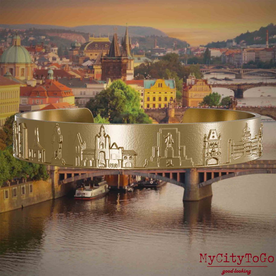 Armreif aus vergoldetem Edelstahl mit Reliefs bekannter Sehenswürdigkeiten der Stadt Prag. Den Hintergrund bildet eine Ansicht der Stadt Prag.