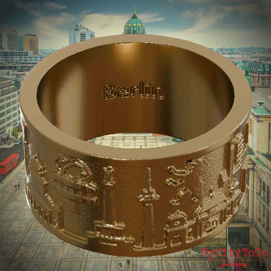 Ring aus vergoldetem Edelstahl mit Reliefs bekannter Sehenswürdigkeiten der Stadt Berlin und einer Gravur des Stadtnamens auf der Innenseite. Den Hintergrund bildet eine Ansicht der Stadt Berlin. 