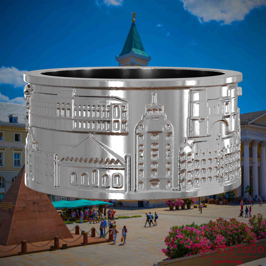 Silberner Ring mit Reliefs bekannter Sehenswürdigkeiten der Stadt Karlsruhe. Den Hintergrund bildet eine Ansicht der Stadt Karlsruhe.