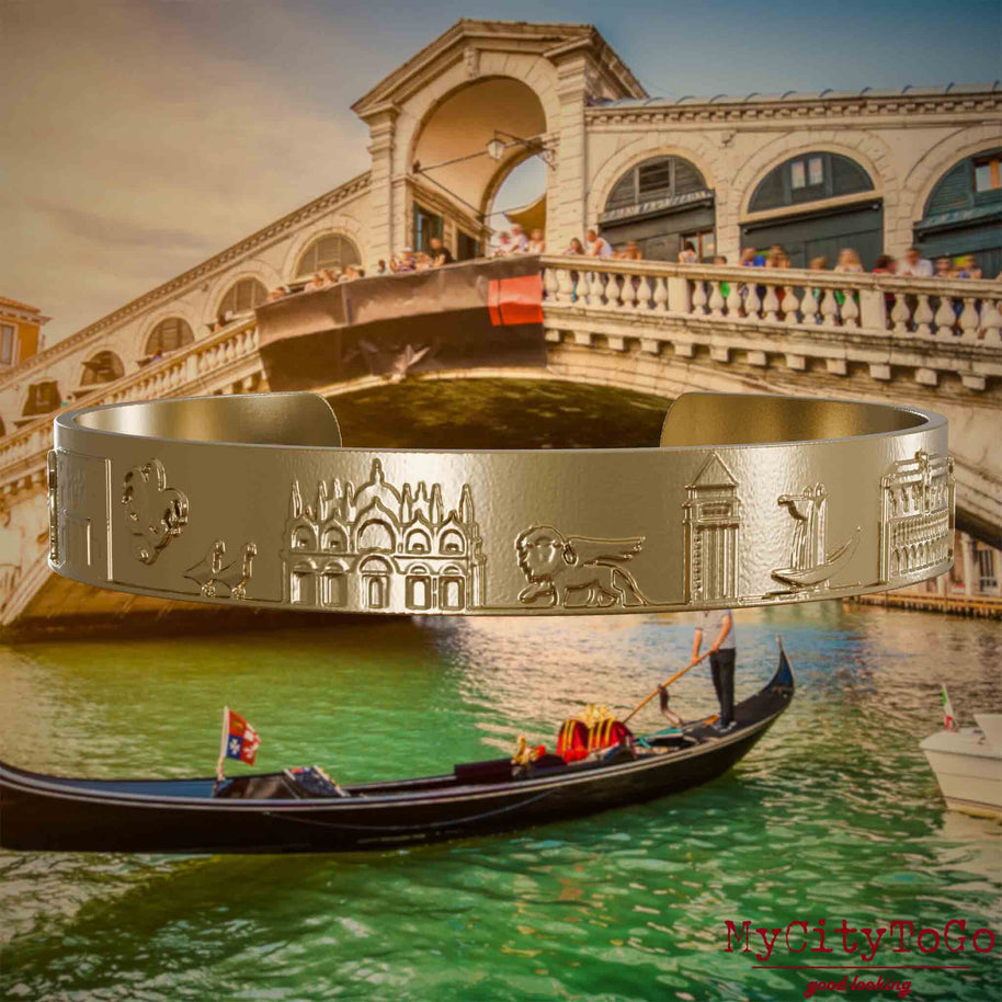 Armreif aus vergoldetem Edelstahl mit Reliefs bekannter Sehenswürdigkeiten der Stadt Venedig. Den Hintergrund bildet eine Ansicht der Stadt Venedig.