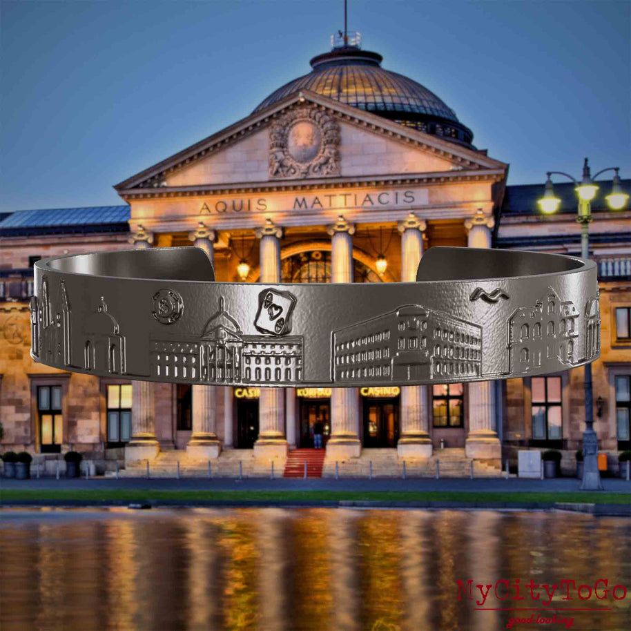 Bangle made of titanium with reliefs of well-known landmarks of the city of Wiesbaden. The background features a view of the city of Wiesbaden.