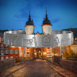 Armreif aus Edelstahl mit Reliefs bekannter Sehenswürdigkeiten der Stadt Heidelberg. Den Hintergrund bildet eine Ansicht der Stadt Heidelberg.