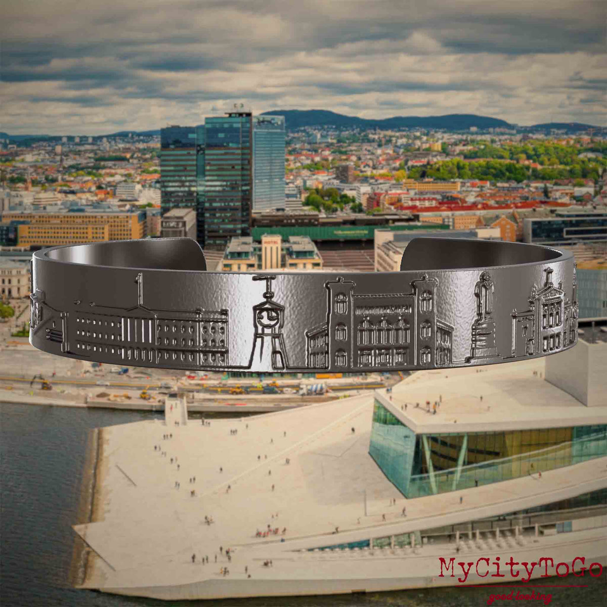 Armreif aus Titan mit Reliefs bekannter Sehenswürdigkeiten der Stadt Oslo. Den Hintergrund bildet eine Ansicht der Stadt Oslo.