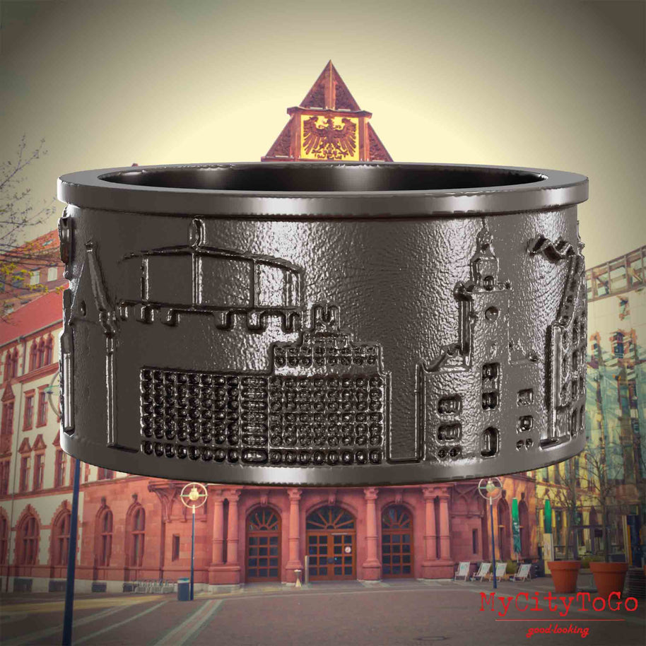 Ring aus Titan mit Reliefs bekannter Sehenswürdigkeiten der Stadt Dortmund. Den Hintergrund bildet eine Ansicht der Stadt Dortmund.
