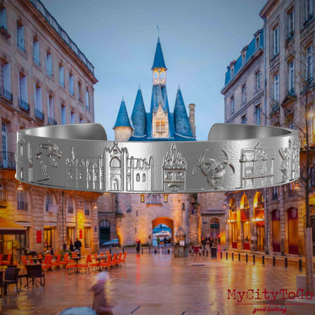 Armreif aus Edelstahl mit Reliefs bekannter Sehenswürdigkeiten der Stadt Bordeaux. Den Hintergrund bildet eine Ansicht der Stadt Bordeaux.