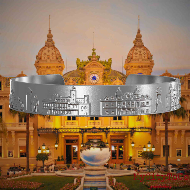 Armreif aus Edelstahl mit Reliefs bekannter Sehenswürdigkeiten der Stadt Monte Carlo. Den Hintergrund bildet eine Ansicht der Stadt Monte Carlo.