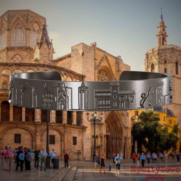 Armreif aus Titan mit Reliefs bekannter Sehenswürdigkeiten der Stadt Valencia. Den Hintergrund bildet eine Ansicht der Stadt Valencia.