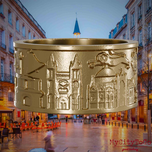 Ring aus vergoldetem Edelstahl mit Reliefs bekannter Sehenswürdigkeiten der Stadt Bordeaux. Den Hintergrund bildet eine Ansicht der Stadt Bordeaux.
