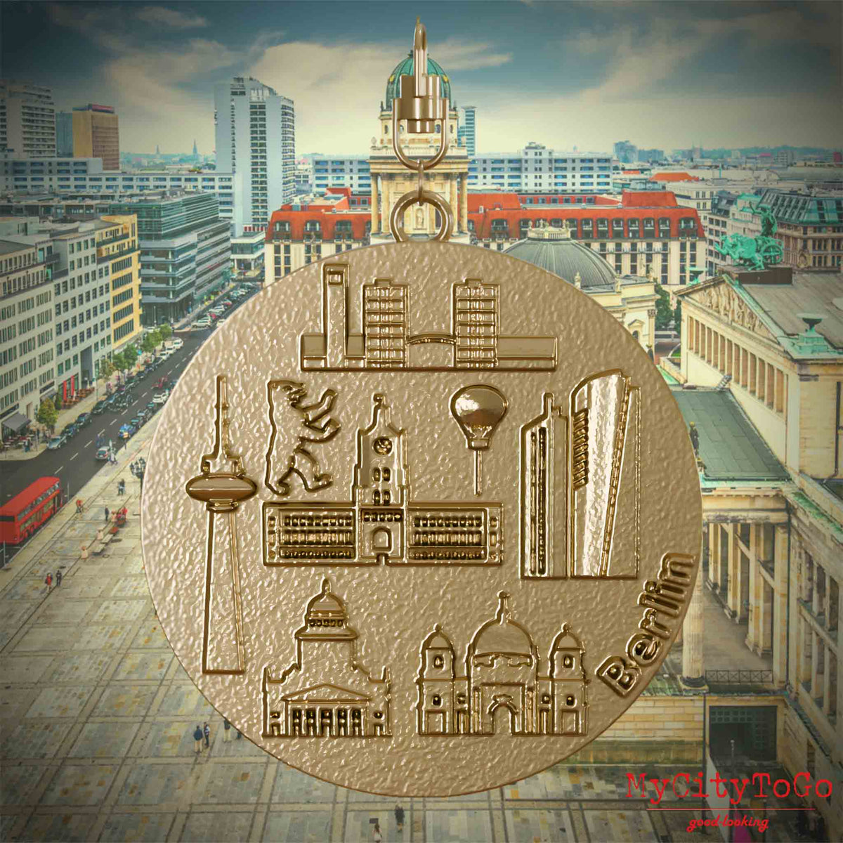 Halskette mit Drehwirbel und Vorderseite eines Schmuckanhängers aus vergoldetem Edelstahl, auf dem Reliefs bekannter Sehenswürdigkeiten der Stadt Berlin abgebildet sind. Den Hintergrund bildet eine Ansicht der Stadt Berlin.