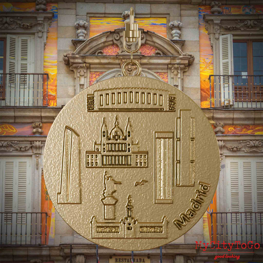 Halskette mit Drehwirbel und Rückseite eines Schmuckanhängers aus vergoldetem Edelstahl, auf dem Reliefs bekannter Sehenswürdigkeiten der Stadt Madrid abgebildet sind. Den Hintergrund bildet eine Ansicht der Stadt Madrid.
