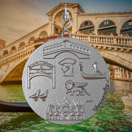 Halskette mit Drehwirbel und Vorderseite eines Schmuckanhängers aus Edelstahl, auf dem Reliefs bekannter Sehenswürdigkeiten der Stadt Venedig abgebildet sind. Den Hintergrund bildet eine Ansicht der Stadt Venedig.
