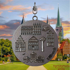 Halskette mit Drehwirbel und Vorderseite eines Schmuckanhängers aus Titan, auf dem Reliefs bekannter Sehenswürdigkeiten der Stadt Luebeck abgebildet sind. Den Hintergrund bildet eine Ansicht der Stadt Luebeck.
