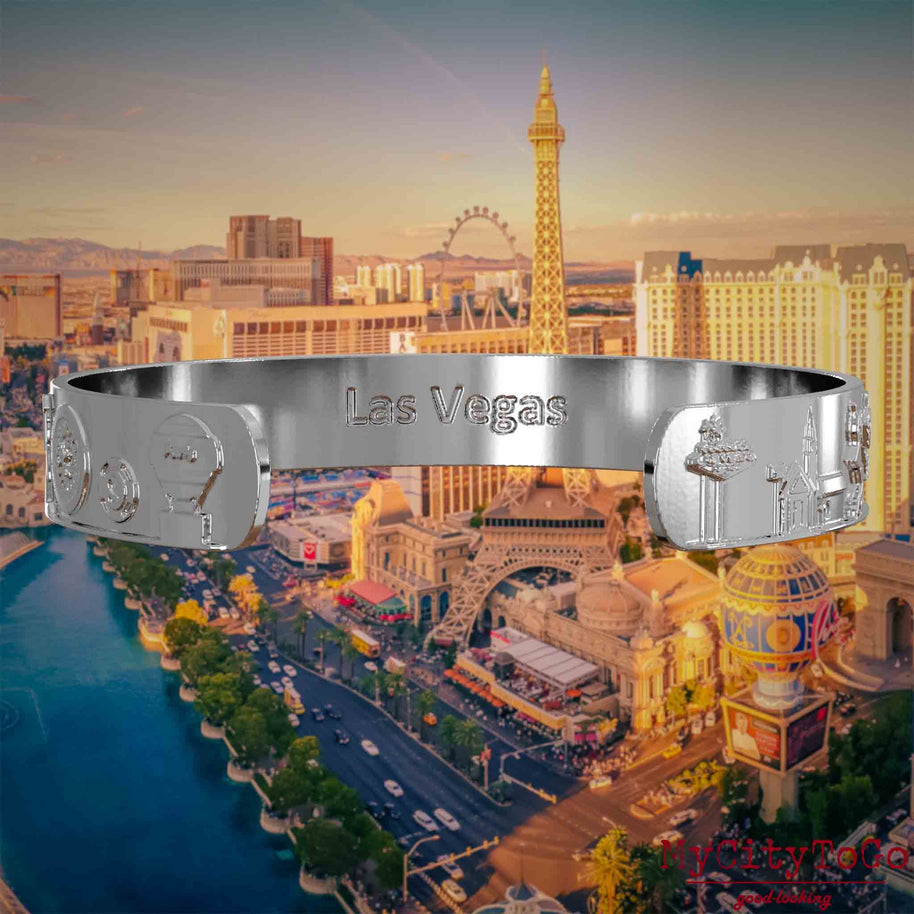 Innenseite eines silbernen Armreifs mit Reliefs bekannter Sehenswürdigkeiten der Stadt Las Vegas und einer Gravur des Stadtnamens. Den Hintergrund bildet eine Ansicht der Stadt Las Vegas.
