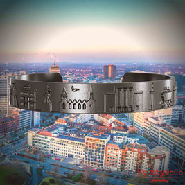 Armreif aus Titan mit Reliefs bekannter Sehenswürdigkeiten der Stadt Essen. Den Hintergrund bildet eine Ansicht der Stadt Essen.