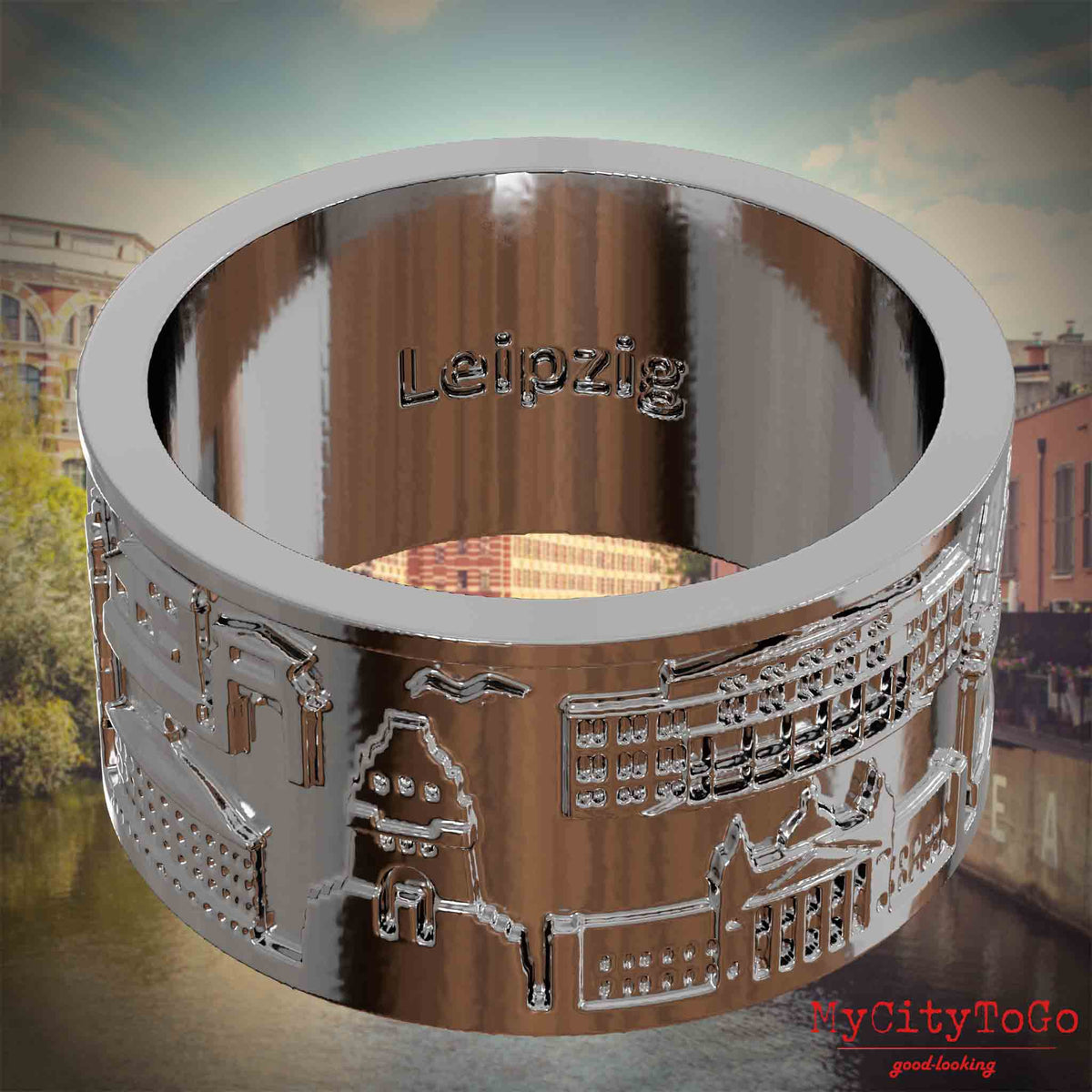 Versilberter Ring mit Reliefs bekannter Sehenswürdigkeiten der Stadt Leipzig und einer Gravur des Stadtnamens auf der Innenseite. Den Hintergrund bildet eine Ansicht der Stadt Leipzig.