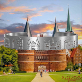 Armreif aus Edelstahl mit Reliefs bekannter Sehenswürdigkeiten der Stadt Luebeck. Den Hintergrund bildet eine Ansicht der Stadt Luebeck.