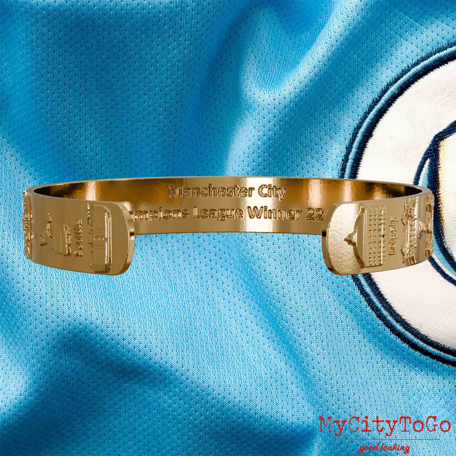 Innenseite eines vergoldeten Armreifs mit Reliefs der Stadien und Sehenswürdigkeiten der Spielorte während der Champions-League-Saison 22/23 von Manchester City und einer Gravur