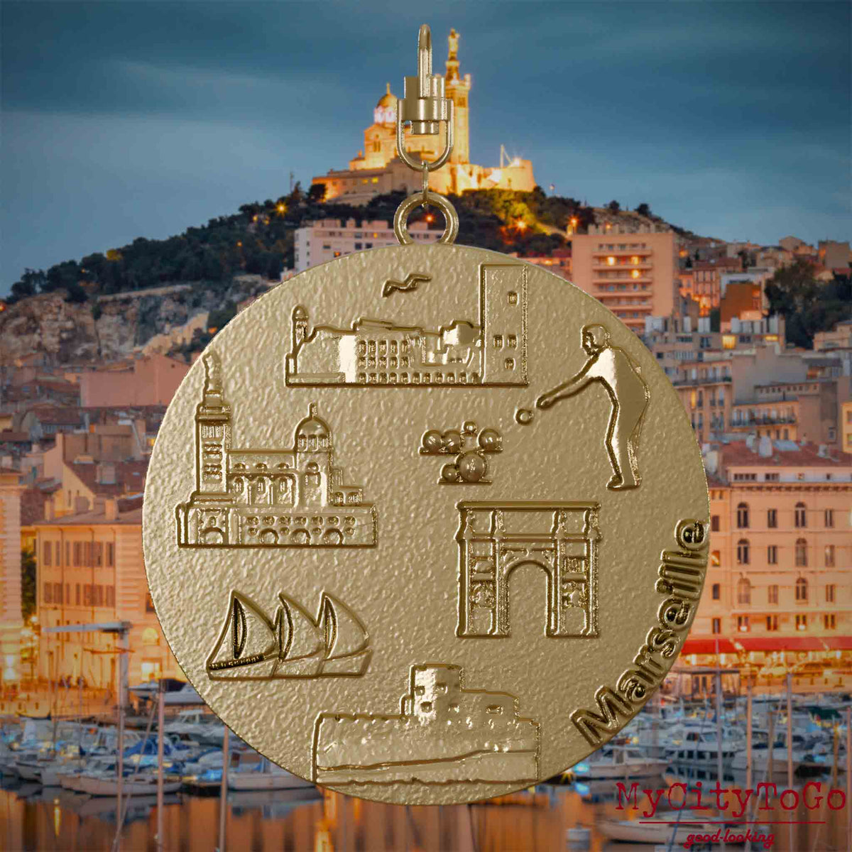 Halskette mit Drehwirbel und Vorderseite eines Schmuckanhängers aus vergoldetem Edelstahl, auf dem Reliefs bekannter Sehenswürdigkeiten der Stadt Marseille abgebildet sind. Den Hintergrund bildet eine Ansicht der Stadt Marseille.
