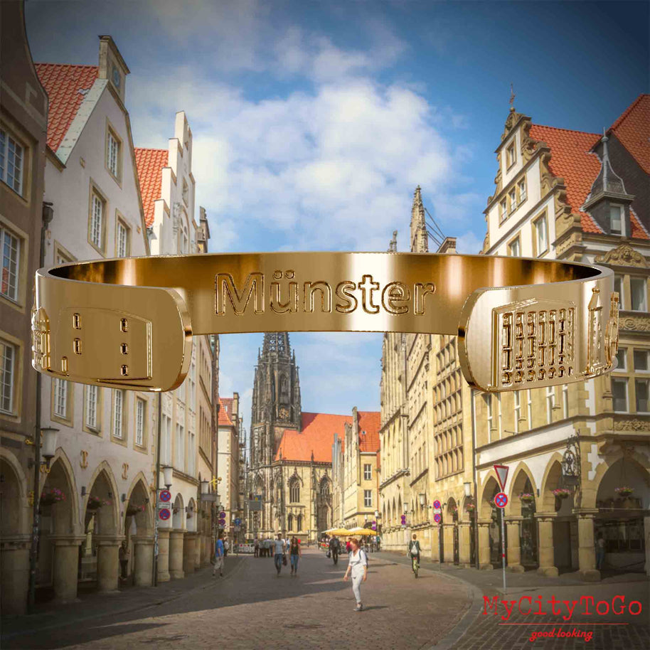 Innenseite eines vergoldeten Armreifs mit Reliefs bekannter Sehenswürdigkeiten der Stadt Muenster und einer Gravur des Stadtnamens. Den Hintergrund bildet eine Ansicht der Stadt Muenster.
