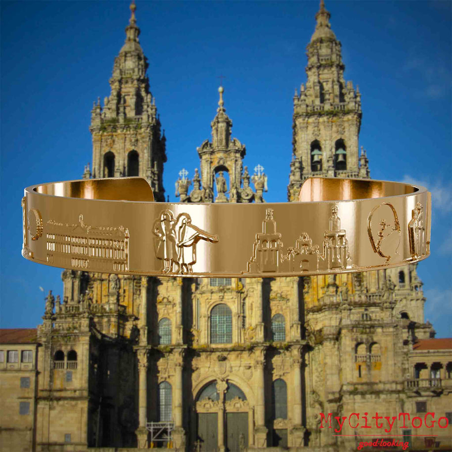 Vergoldeter Armreif mit Reliefs bekannter Sehenswürdigkeiten und Elemente des Jakobsweges. Den Hintergrund bildet die Kathedrale von Santiago de Compostela.