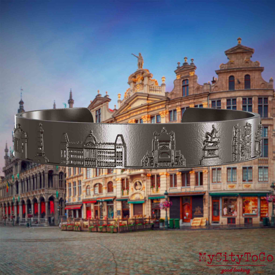 Armreif aus Titan mit Reliefs bekannter Sehenswürdigkeiten der Stadt Brüssel. Den Hintergrund bildet eine Ansicht der Stadt Bruessel.