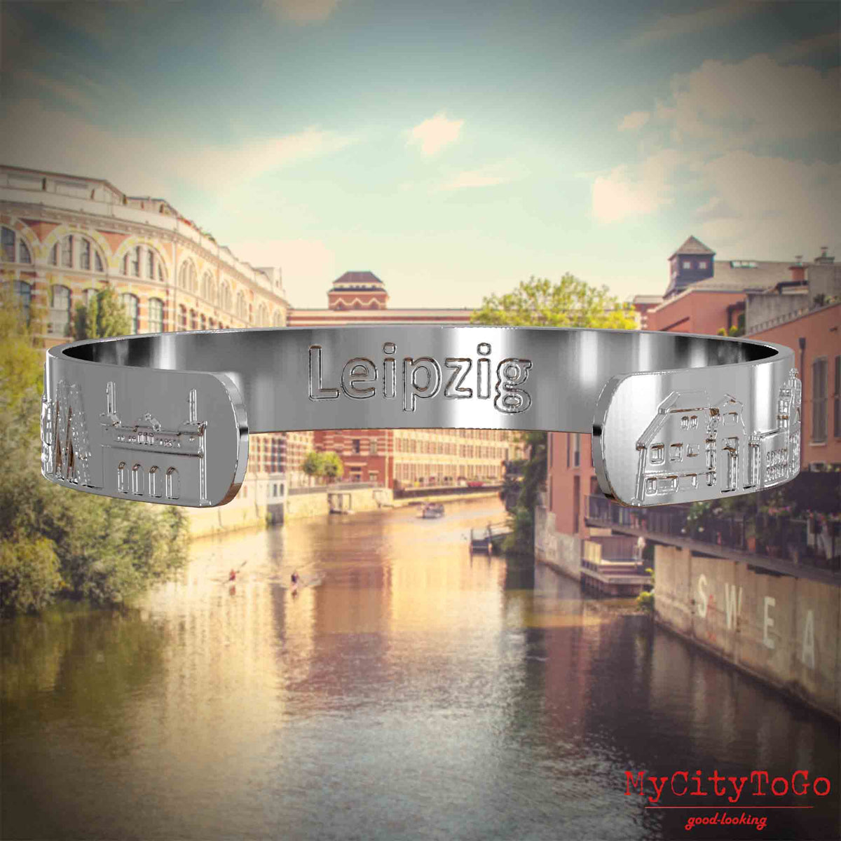 Innenseite eines silbernen Armreifs mit Reliefs bekannter Sehenswürdigkeiten der Stad Leipzig und einer Gravur des Stadtnamens. Den Hintergrund bildet eine Ansicht der Stadt Leipzig.