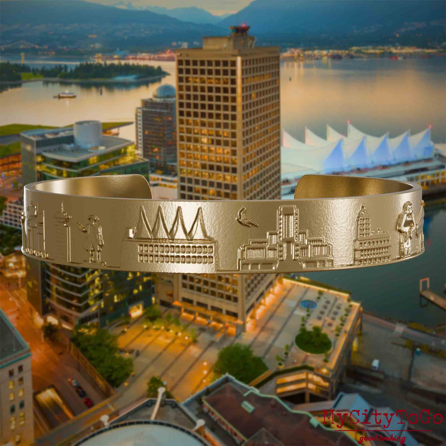 Armreif aus vergoldetem Edelstahl mit Reliefs bekannter Sehenswürdigkeiten der Stadt Vancouver. Den Hintergrund bildet eine Ansicht der Stadt Vancouver.