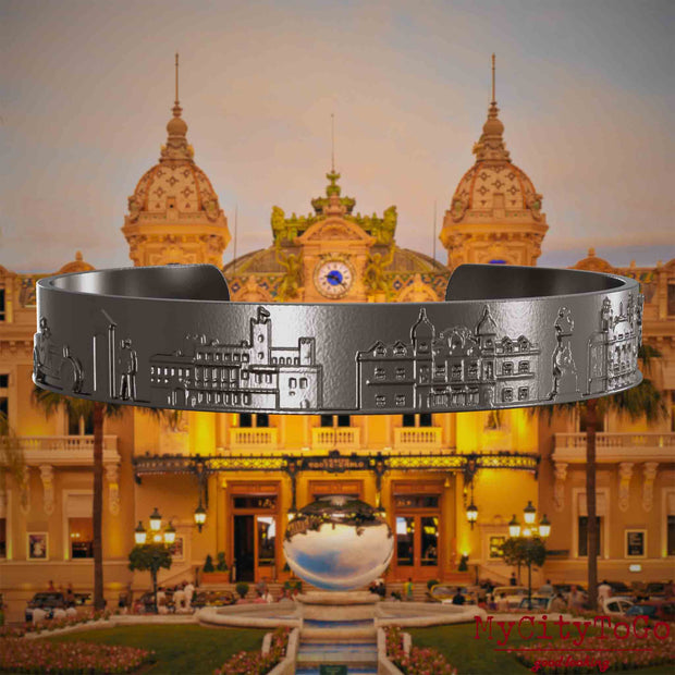 Armreif aus Titan mit Reliefs bekannter Sehenswürdigkeiten der Stadt Monte Carlo. Den Hintergrund bildet eine Ansicht der Stadt Monte Carlo.