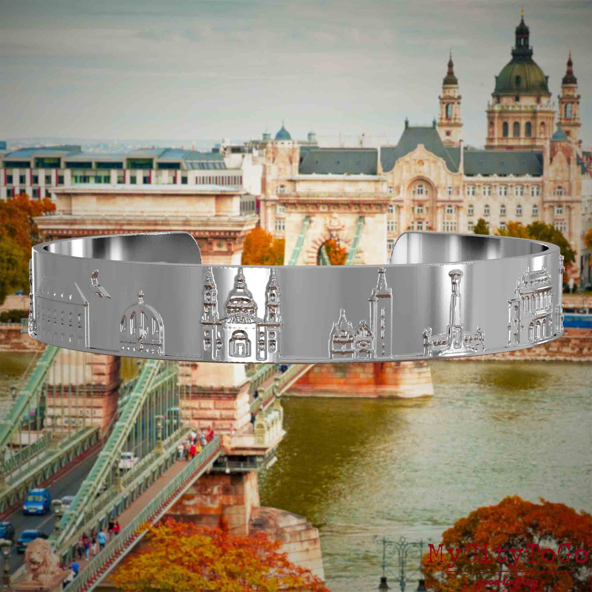 Versilberter Armreif mit Reliefs bekannter Sehenswürdigkeiten der Stadt Budapest. Den Hintergrund bildet eine Ansicht der Stadt Budapest.