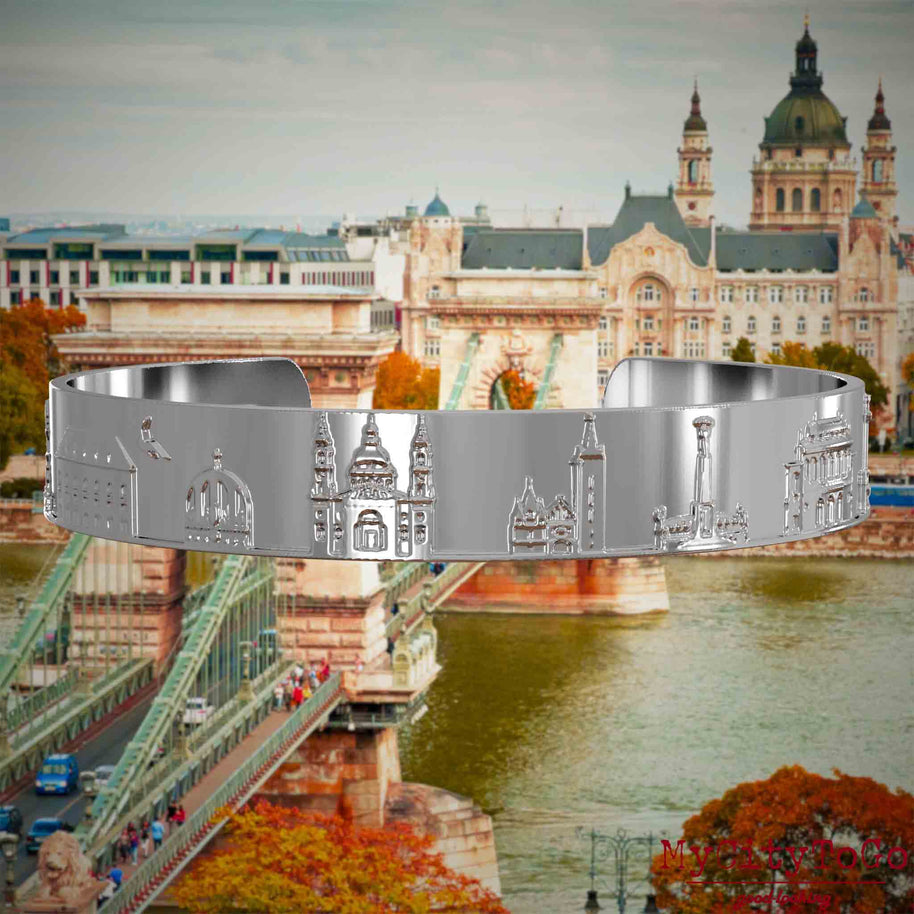 Versilberter Armreif mit Reliefs bekannter Sehenswürdigkeiten der Stadt Budapest. Den Hintergrund bildet eine Ansicht der Stadt Budapest.