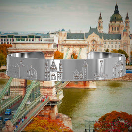 Versilberter Armreif mit Reliefs bekannter Sehenswürdigkeiten der Stadt Budapest. Den Hintergrund bildet eine Ansicht der Stadt Budapest.