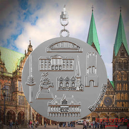 Halskette mit Drehwirbel und Vorderseite eines silbernen Schmuckanhängers, auf dem Reliefs bekannter Sehenswürdigkeiten der Stadt Bremen abgebildet sind. Den Hintergrund bildet eine Ansicht der Stadt Bremen.