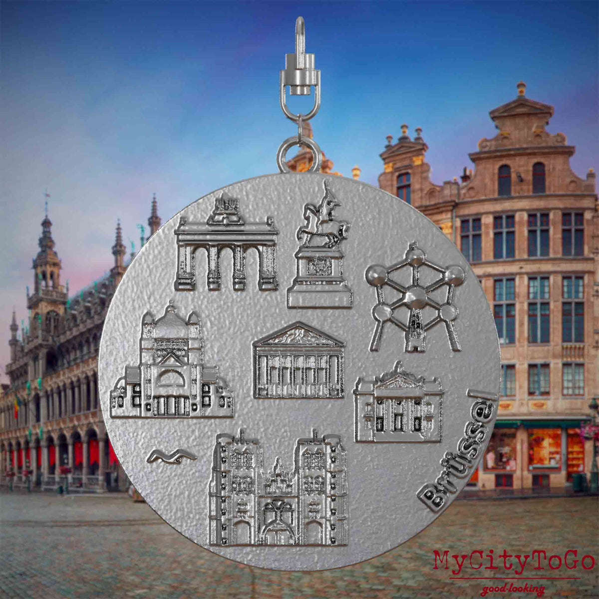 Halskette mit Drehwirbel und Rückseite eines Schmuckanhängers aus Edelstahl, auf dem Reliefs bekannter Sehenswürdigkeiten der Stadt Bruessel abgebildet sind. Den Hintergrund bildet eine Ansicht der Stadt Bruessel.

