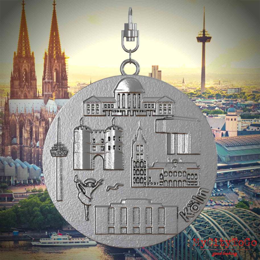 Halskette mit Drehwirbel und Rückseite eines Schmuckanhängers aus Edelstahl, auf dem Reliefs bekannter Sehenswürdigkeiten der Stadt Koeln abgebildet sind. Den Hintergrund bildet eine Ansicht der Stadt Koeln.