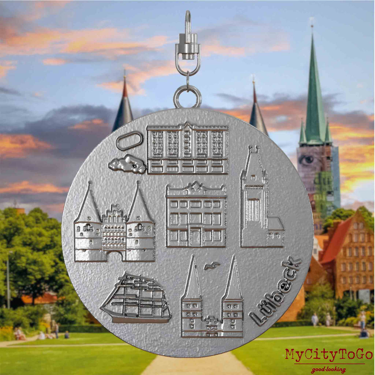 Halskette mit Drehwirbel und Rückseite eines Schmuckanhängers aus Edelstahl, auf dem Reliefs bekannter Sehenswürdigkeiten der Stadt Luebeck abgebildet sind. Den Hintergrund bildet eine Ansicht der Stadt Luebeck.
