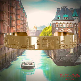 Gold-plated Bangle with reliefs of well-known landmarks of the city of Hamburg. The background features a view of the city of Hamburg.