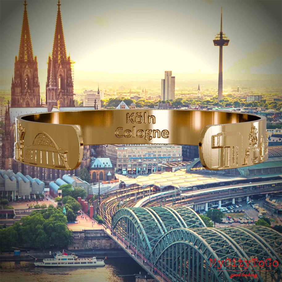 Innenseite eines vergoldeten Armreifs mit Reliefs bekannter Sehenswürdigkeiten der Stadt Köln und einer Gravur des Stadtnamens. Den Hintergrund bildet eine Ansicht der Stadt Koeln.