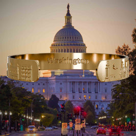 Innenseite eines vergoldeten Armreifs mit Reliefs bekannter Sehenswürdigkeiten der Stadt Washington und einer Gravur des Stadtnamens. Den Hintergrund bildet eine Ansicht der Stadt Washington.