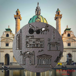 Halskette mit Drehwirbel und Vorderseite eines Schmuckanhängers aus Titan, auf dem Reliefs bekannter Sehenswürdigkeiten der Stadt Wien abgebildet sind. Den Hintergrund bildet eine Ansicht der Stadt Wien.
