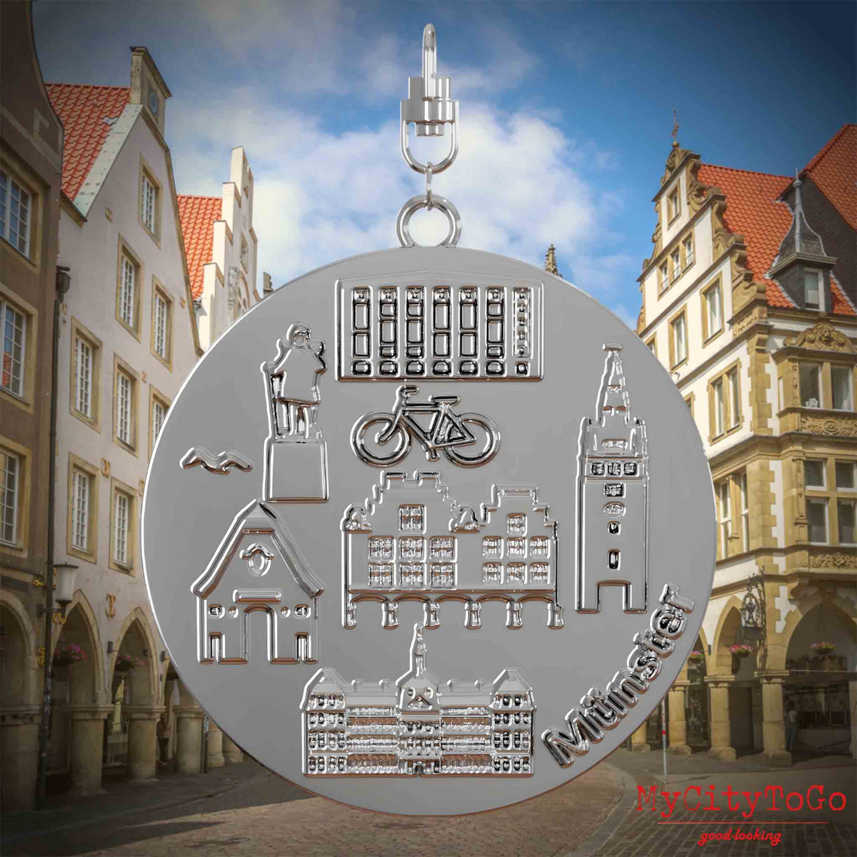 Halskette mit Drehwirbel und Rückseite eines silbernen Schmuckanhängers, auf dem Reliefs bekannter Sehenswürdigkeiten der Stadt Muenster abgebildet sind. Den Hintergrund bildet eine Ansicht der Stadt Muenster.