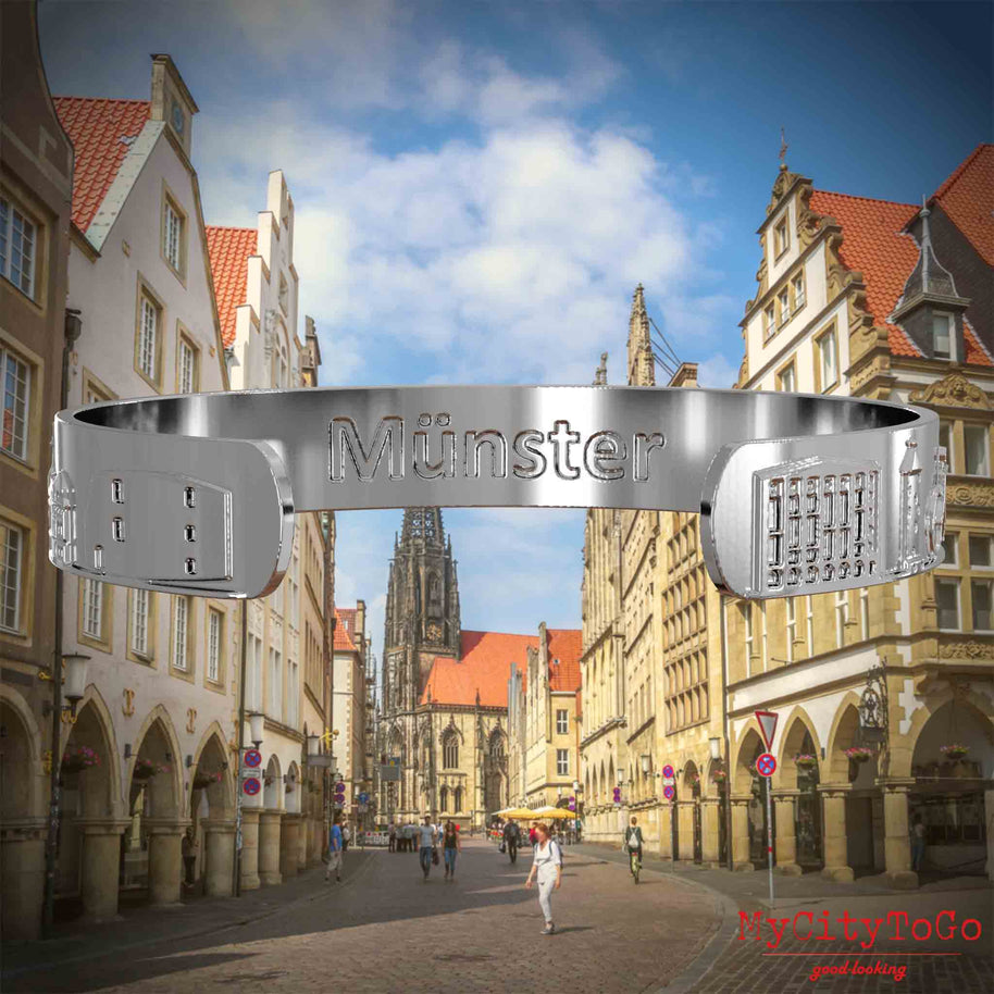 Innenseite eines silbernen Armreifs mit Reliefs bekannter Sehenswürdigkeiten der Stadt Muenster und einer Gravur des Stadtnamens. Den Hintergrund bildet eine Ansicht der Stadt Muenster.