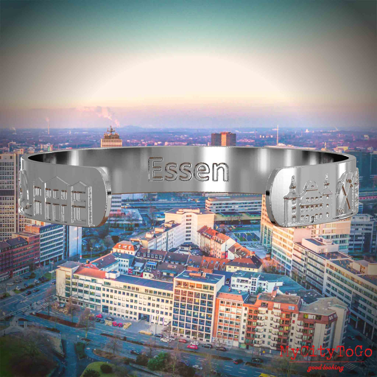 Innenseite eines silbernen Armreifs mit Reliefs bekannter Sehenswürdigkeiten der Stadt Essen und einer Gravur des Stadtnamens. Den Hintergrund bildet eine Ansicht der Stadt Essen.