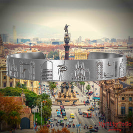 Armreif aus Edelstahl mit Reliefs bekannter Sehenswürdigkeiten der Stadt Barcelona. Den Hintergrund bildet eine Ansicht der Stadt Barcelona.