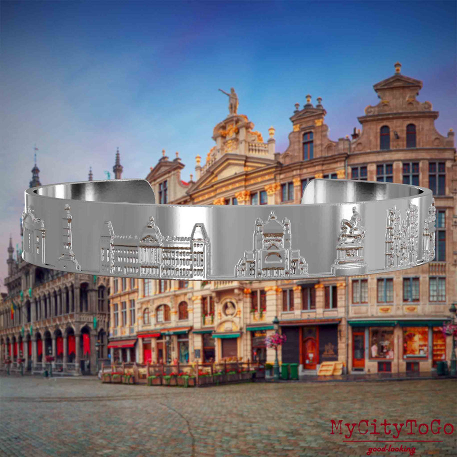 Versilberter Armreif mit Reliefs bekannter Sehenswürdigkeiten der Stadt Brüssel. Den Hintergrund bildet eine Ansicht der Stadt Bruessel.