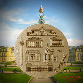 Halskette mit Drehwirbel und Vorderseite eines Schmuckanhängers aus vergoldetem Edelstahl, auf dem Reliefs bekannter Sehenswürdigkeiten der Stadt Stuttgart abgebildet sind. Den Hintergrund bildet eine Ansicht der Stadt Stuttgart.
