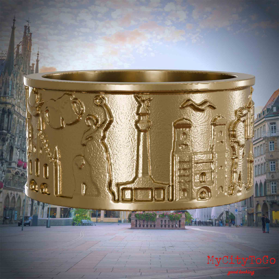 Ring aus vergoldetem Edelstahl mit Reliefs bekannter Sehenswürdigkeiten der Stadt Muenchen. Den Hintergrund bildet eine Ansicht der Stadt Muenchen.